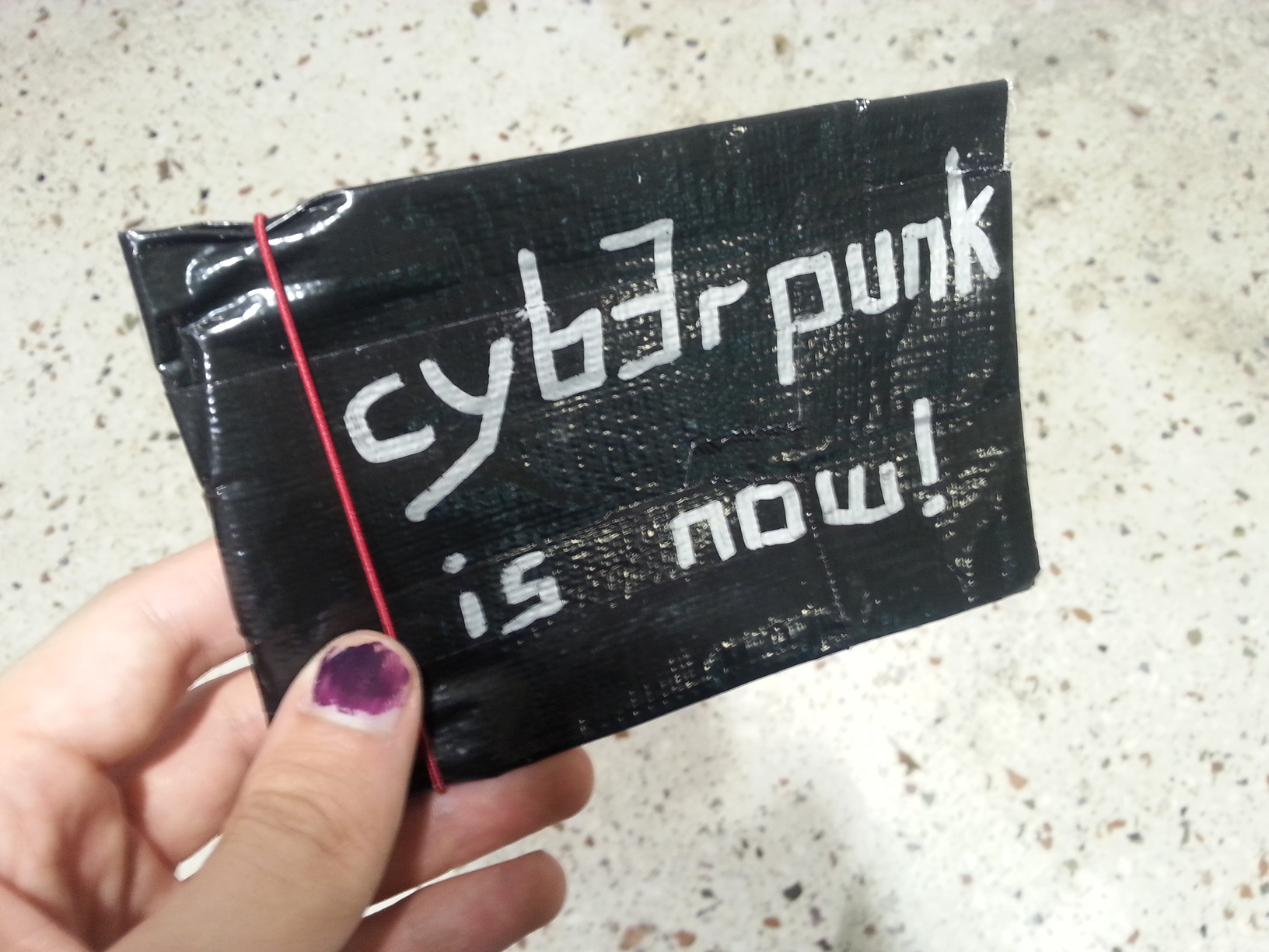 Eine Handy-große Tasche aus einem silbrigen Material, darauf steht 'cyberpunk is now'.